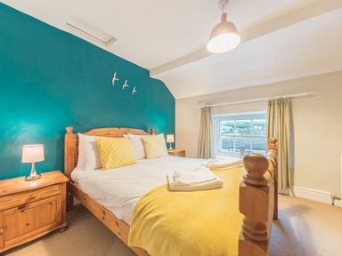A bedroom with a wooden bed frame yellow pillows and blanket blue accent wall and two bedside tables with lamps at Abbey Farm House in St Bees