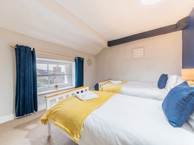 A bedroom with two single beds with yellow throws and blue cushions and a window with blue curtains at Abbey Farm House in St Bees