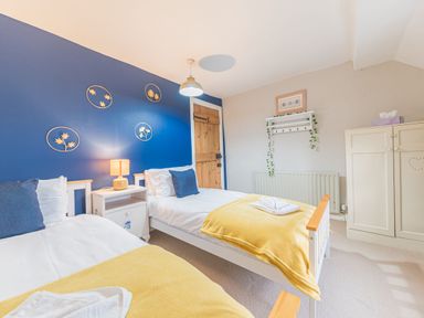 A bedroom with two single beds yellow blankets a nightstand with lamp and blue accent wall with wall decorations at Abbey Farm House in St Bees