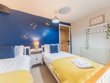 A bedroom with two single beds with yellow blankets and blue pillows a nightstand with a lamp and wooden door at Abbey Farm House in St Bees