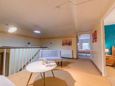 A landing area with a white table, a sofa, wall paintings, and a view into bedrooms at Abbey Farm House in St Bees