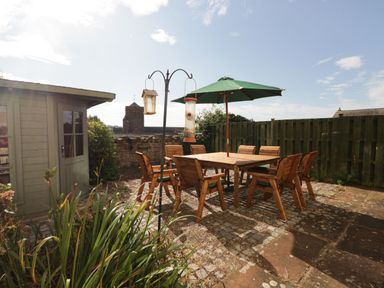 An outdoor patio with wooden table and chairs under a green umbrella near a wooden shed at Abbey Farm House in St Bees