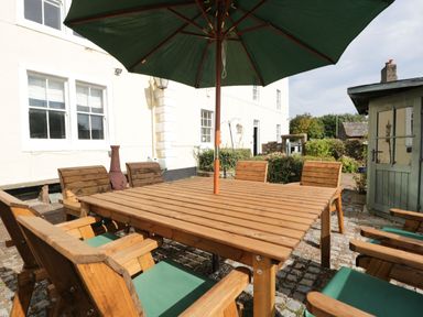 An outdoor patio with a wooden table and chairs under a green umbrella at Abbey Farm House in St Bees
