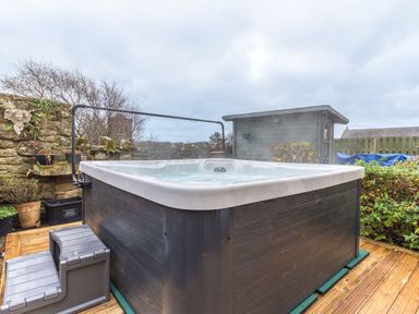 An outdoor hot tub on a wooden deck with potted plants and stone wall at Abbey Farm House in St Bees