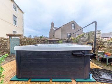 A hot tub on a wooden deck in a courtyard with stone walls and potted plants at Abbey Farm House in St Bees