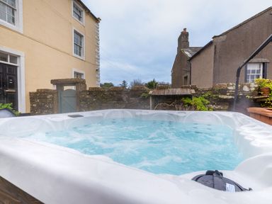 An outdoor hot tub with bubbling water in a yard surrounded by stone walls and buildings at Abbey Farm House in St Bees