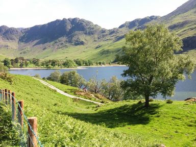 A lake surrounded by green hills and trees with a dirt path and a fence in the foreground at Abbey Farm House in St Bees