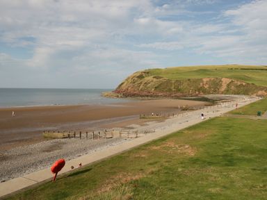 A beach with a concrete walkway grassy area and people walking near a hill at Abbey Farm House in St Bees