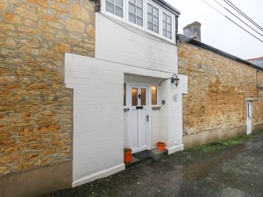 A stone exterior wall with a white entrance door and two small plant pots at Poppy Cottage in Beaminster