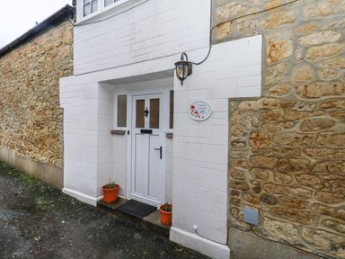 A white door with windows and flower pots beside it set in a stone wall at Poppy Cottage in Beaminster