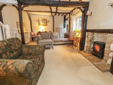 A living room with sofas wood beam ceiling a fireplace and tables at Poppy Cottage in Beaminster