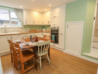 A kitchen with wooden dining table and chairs white cabinets built in oven and green walls at Poppy Cottage in Beaminster