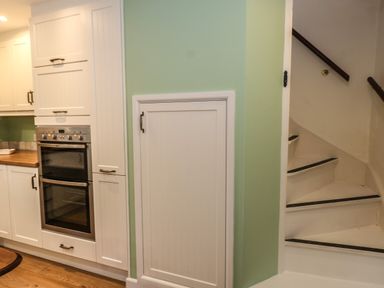 A kitchen with white cabinets double oven wooden countertop and stairs with white risers and dark handrails at Poppy Cottage in Beaminster