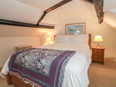 A bedroom with a bed with white bedding and a patterned throw and two bedside tables with lamps at Poppy Cottage in Beaminster