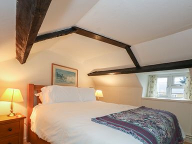 A bedroom with a double bed bedside tables lamps and exposed wooden ceiling beams at Poppy Cottage in Beaminster