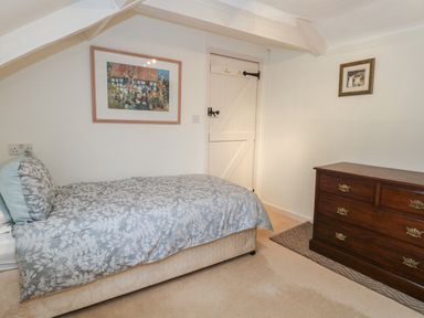 A bedroom with a single bed with floral bedding a wooden dresser and two framed pictures on the walls at Poppy Cottage in Beaminster