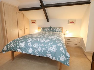 A bedroom with a double bed covered with floral bedding two bedside tables with lamps built-in wardrobes and exposed ceiling beams at Poppy Cottage in Beaminster