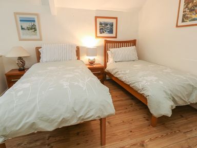 A bedroom with two single beds with striped pillows and floral bedspreads with two wooden bedside tables and lamps at Poppy Cottage in Beaminster