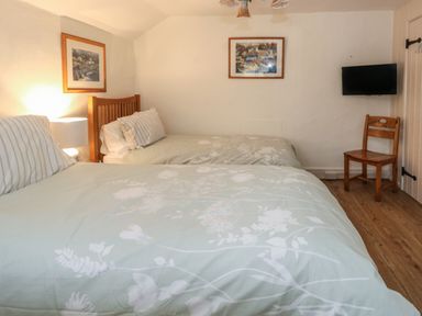 A bedroom with two single beds a wooden chair a mounted TV and framed pictures on white walls at Poppy Cottage in Beaminster