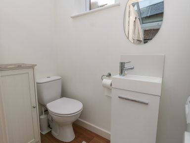 A bathroom with a toilet sink cabinet mirror and a small window at Poppy Cottage in Beaminster