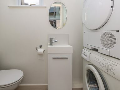 A laundry room with a washing machine, dryer, sink, toilet, and a wall mirror at Poppy Cottage in Beaminster