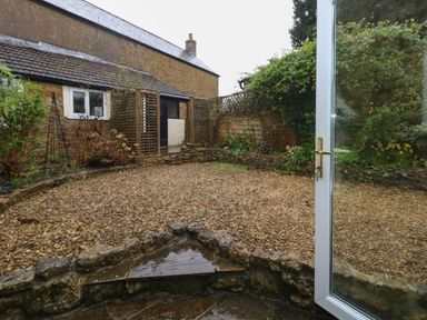 A garden with gravel ground plants and a stone wall viewed through an open glass door at Poppy Cottage in Beaminster
