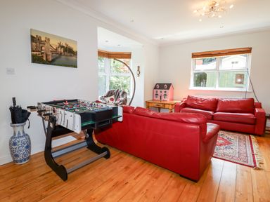 A living room with red leather sofas a foosball table and a dollhouse on a wooden table at Trem Y Don in Dolgarrog