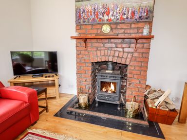A living room with a brick fireplace with a wood-burning stove and firewood at Trem Y Don in Dolgarrog