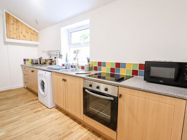 A kitchen with wooden cabinets a washing machine an oven a stovetop a microwave and a window at Trem Y Don in Dolgarrog