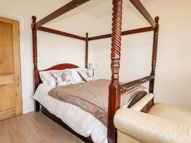 A bedroom with a wooden four-poster bed a beige armchair and a lamp near the bed at Trem Y Don in Dolgarrog