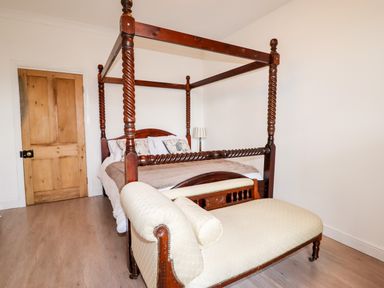 A bedroom with a wooden four-poster bed and an upholstered chaise lounge at Trem Y Don in Dolgarrog