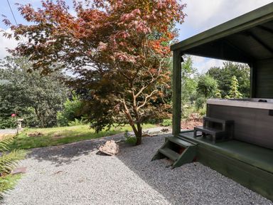 An outdoor area with a covered hot tub next to a tree and gravel ground at Trem Y Don in Dolgarrog