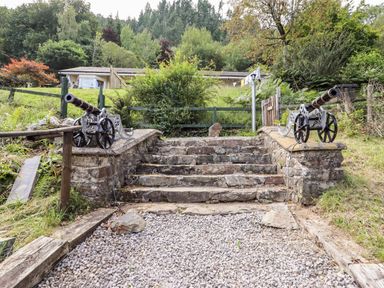 Stone steps between two decorative cannons with greenery and a fence in the background at Trem Y Don in Dolgarrog