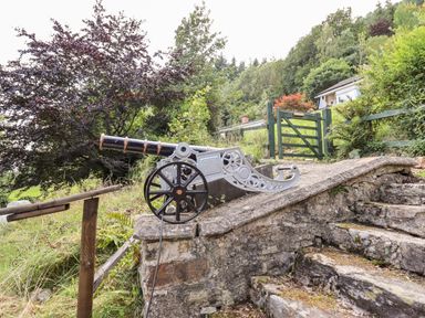 A path with a decorative cannon on a stone platform and green gate in a garden at Trem Y Don in Dolgarrog