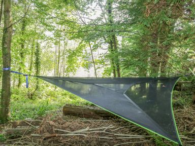 A black triangular hammock tied between two trees in a forest at Trem Y Don in Dolgarrog