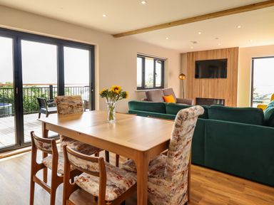 A dining table with chairs and a vase of sunflowers next to a living area with sofas a TV and large windows at Mynydd Y Glyn Lodge in Llanfyllin near Llanrhaeadr-Ym-Mochnant