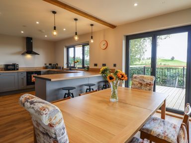 A kitchen and dining area with wooden table and floral chairs next to sliding glass doors at Mynydd Y Glyn Lodge in Llanfyllin near Llanrhaeadr-Ym-Mochnant