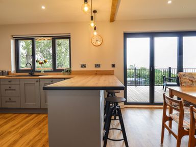 A kitchen with stools at a counter next to sliding glass doors and a dining table with chairs at Mynydd Y Glyn Lodge in Llanfyllin near Llanrhaeadr Ym Mochnant