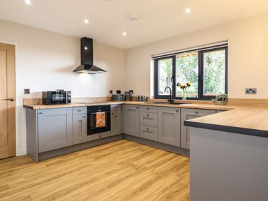 A kitchen with grey cabinets wooden countertops a black oven and stove a microwave and a window with a vase of flowers at Mynydd Y Glyn Lodge in Llanfyllin near Llanrhaeadr-Ym-Mochnant