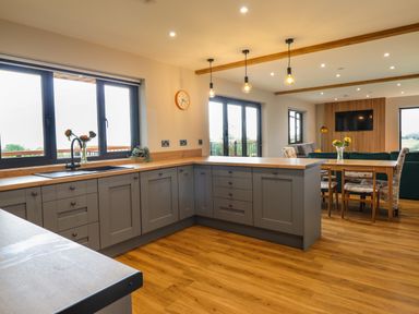 A kitchen with gray cabinets and wooden countertops open to a dining area with a wooden table and floral chairs at Mynydd Y Glyn Lodge in Llanfyllin near Llanrhaeadr-Ym-Mochnant