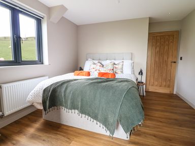 A bedroom with a bed green blanket and orange towels near a window and wooden door at Mynydd Y Glyn Lodge in Llanfyllin near Llanrhaeadr-Ym-Mochnant
