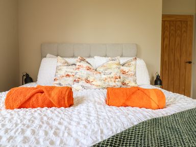 A bed with white bedding orange towels and patterned pillows in a bedroom with a wooden door at Mynydd Y Glyn Lodge in Llanfyllin near Llanrhaeadr-Ym-Mochnant