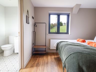 A bedroom with a bed covered in a green blanket and orange towels near a window and an open bathroom with a toilet at Mynydd Y Glyn Lodge in Llanfyllin near Llanrhaeadr-Ym-Mochnant