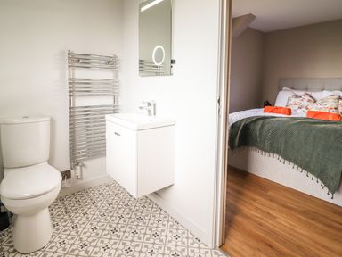 A bathroom with a toilet sink towel rack and patterned floor tiles next to a bedroom with a bed and orange towels at Mynydd Y Glyn Lodge in Llanfyllin near Llanrhaeadr-Ym-Mochnant