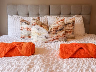 A bed with patterned pillows and rolled orange towels on a white textured bedspread at Mynydd Y Glyn Lodge in Llanfyllin near Llanrhaeadr-Ym-Mochnant