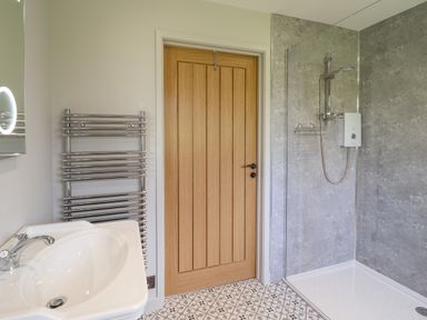 A bathroom with a white sink a wooden door a chrome towel radiator and a walk in shower at Mynydd Y Glyn Lodge Llanfyllin near Llanrhaeadr-Ym-Mochnant