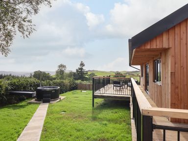A wooden lodge with a deck and outdoor seating on a grassy lawn with a hot tub at Mynydd Y Glyn Lodge in Llanfyllin near Llanrhaeadr-Ym-Mochnant