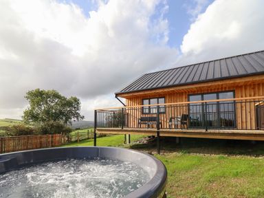 An outdoor hot tub near a wooden lodge with a deck and seating at Mynydd Y Glyn Lodge in Llanfyllin near Llanrhaeadr-Ym-Mochnant