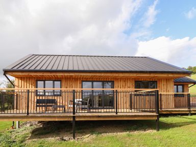 A wooden lodge with a metal roof and a deck with black railings at Mynydd Y Glyn Lodge in Llanfyllin near Llanrhaeadr-Ym-Mochnant