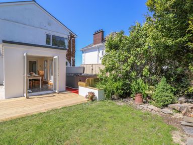 A backyard garden with grass and plants next to a house with open doors leading to a dining area at Towyn Hall in New Quay
